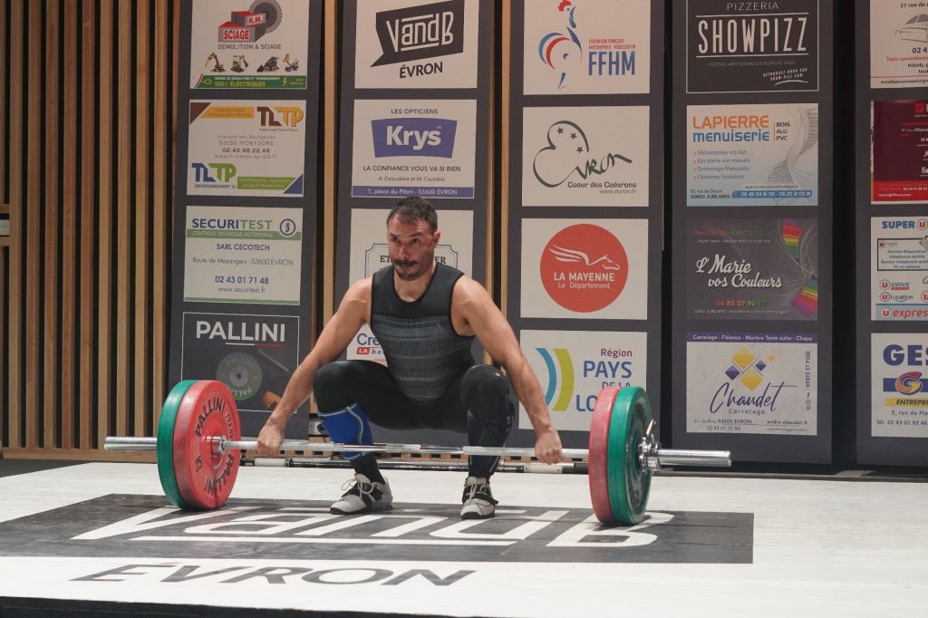 Haltérophile master en position de réception de squat sur plateforme de compétition FFHM